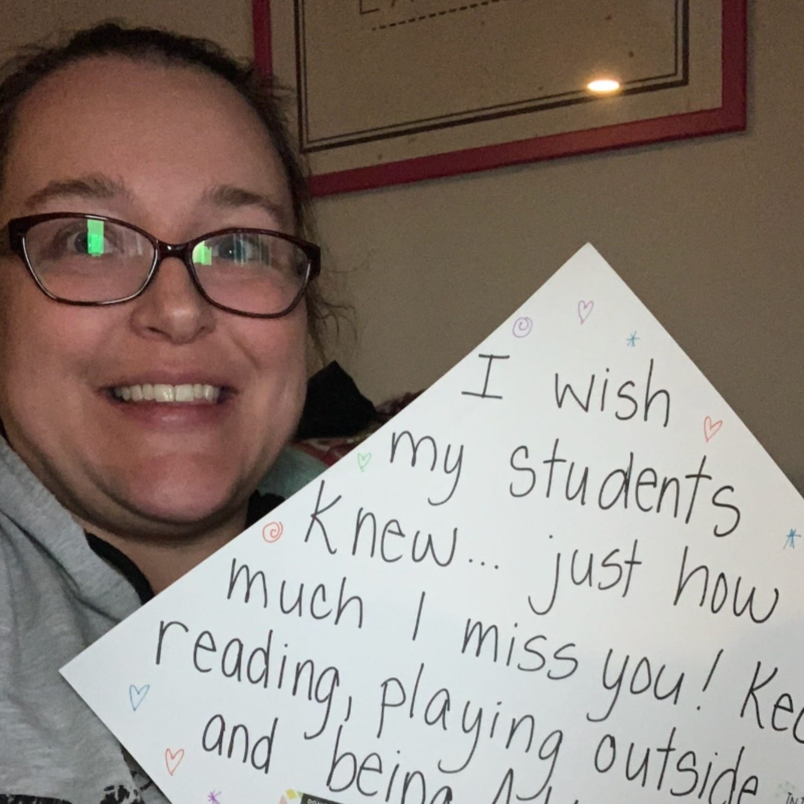 Sarah holding up a sign that says I wish students knew just how much I miss them reading and playing outside.